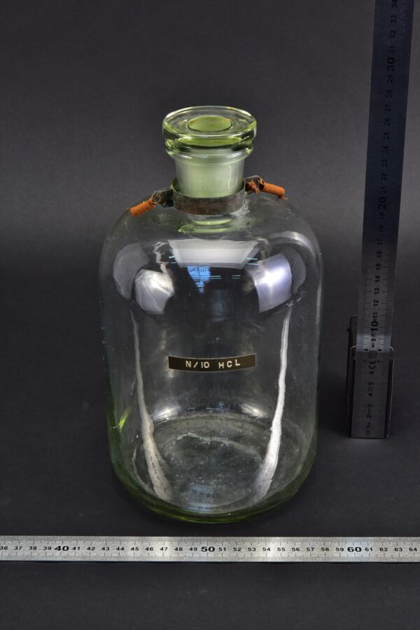 Clear reagent bottle with glass stopper, spring-equipped metal collar and “N/10 HCL” label Clear reagent bottle with glass stopper, spring-equipped metal collar and “N/10 HCL” label